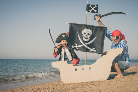 Father and son playing on the beach at the day time. They are dressed in sailor's vests and pirate costumes. Concept of happy game on vacation and friendly family.の写真素材