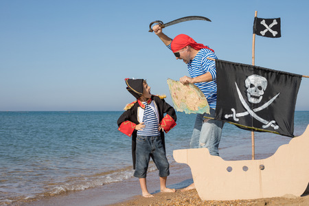Father and son playing on the beach at the day time. They are dressed in sailor's vests and pirate costumes. Concept of happy game on vacation and friendly family.の写真素材