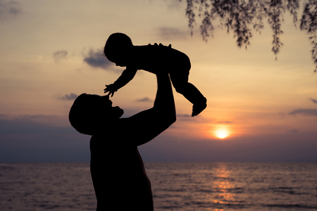 Father and baby son  playing on the beach at the sunset time. People having fun outdoors. Concept of summer vacation and friendly family.の写真素材