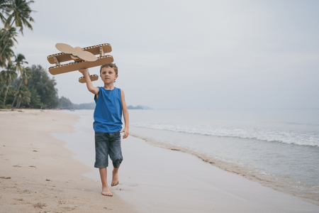 Little boy playing with cardboard toy airplane on the beach at the day time. Concept of happy game. Child having fun outdoors. Picture made on the background of blue sky.の写真素材