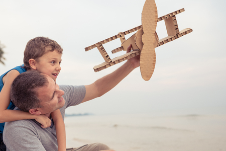 Father and son playing with cardboard toy airplane in the park at the day time. Concept of friendly family. People having fun outdoors on the beach.の写真素材