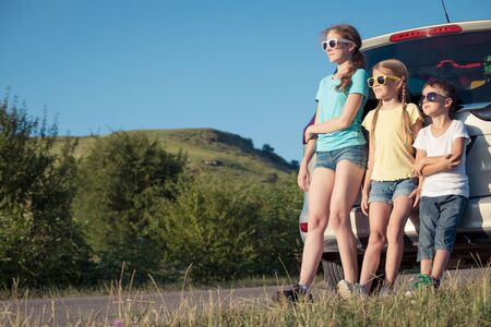 Happy brother and his two sisters are standing near the car at the day time. Children having fun outdoors. Concept of the family is ready for travel.の写真素材