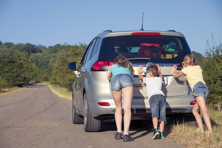 Happy brother and his two sisters are standing near the car at the day time. Children having fun outdoors. Concept of the family is ready for travel.の写真素材
