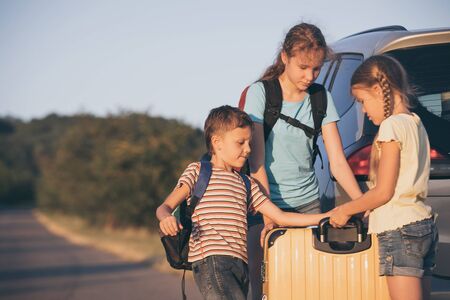 Happy brother and his two sisters are standing near the car at the day time. Children having fun outdoors. Concept of the family is ready for travel.の写真素材