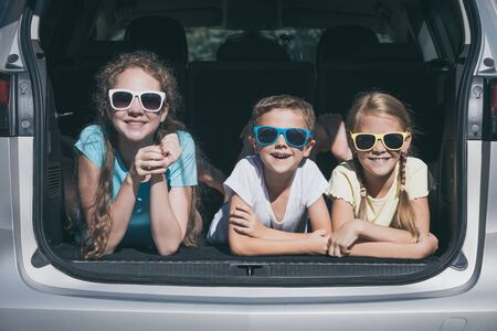 Happy brother and his two sisters are sitting in the car at the day time. Children having fun...