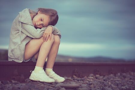 Portrait of young sad girl sitting outdoors  on the railway at the day time. Concept of sorrow.の写真素材