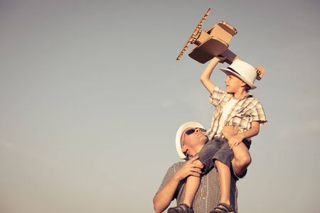 Father and son playing with cardboard toy airplane in the park at the day time. Concept of friendly family. People having fun outdoors. Picture made on the background of blue sky.の写真素材