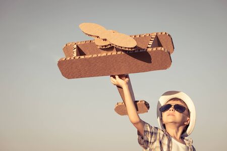 Little boy playing with cardboard toy airplane in the park at the day time. Concept of happy game. Child having fun outdoors. Picture made on the background of blue sky.の写真素材