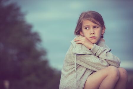 Portrait of young sad girl sitting outdoors  on the railway at the day time. Concept of sorrow.