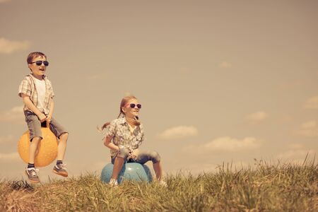 Brother and sister playing on the field at the day time. Children having fun outdoors. They jumping on inflatable balls on the lawn. Concept of friendly family.の写真素材