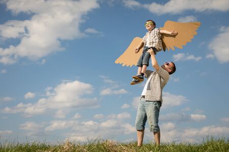 Father and son playing with cardboard toy wings in the park at the day time. Concept of friendly family. People having fun outdoors. Picture made on the background of blue sky.の写真素材