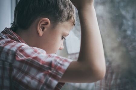 portrait one sad little boy sitting near a window at the day time.の写真素材
