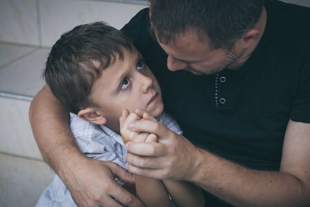 Portrait of young sad little boy and father sitting outdoors at the day time. Concept of sorrow.の写真素材