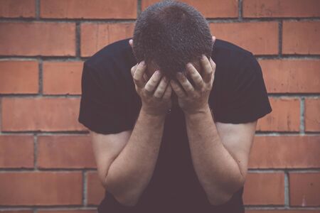 portrait one sad man standing near a wall and covers his face at the dayの写真素材
