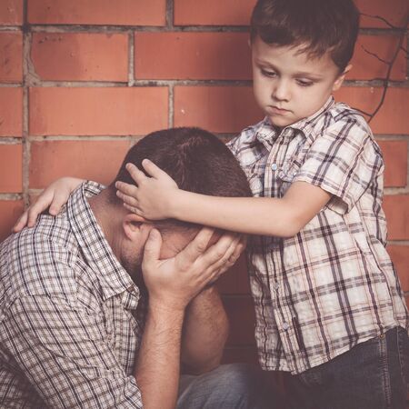 Portrait of young sad little boy and father sitting outdoors at the day time. Concept of sorrow.の写真素材
