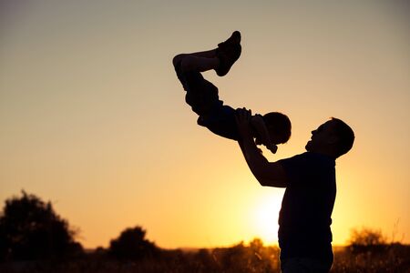 Father and son playing in the park at the sunset time. People having fun on the field. Concept of friendly family and of summer vacation.の写真素材