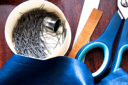 Closeup of sewing workshop tools of scissors rule needle minikin pin leather fabric lying on wooden table thimble for making cloth couture or bespoke with no peopleの写真素材