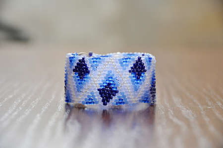 Bracelet fragment from small beads with ethnic ornament on a wooden background, texture and...