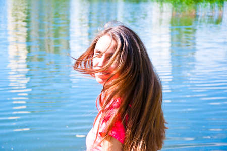 young sexy smiling woman or girl with pretty cute face and long brunette hair in pink shirt near river or sea water sunny outdoor on natural backgroundの写真素材