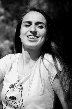 young sexy smiling woman or girl with pretty cute face and long brunette hair in shirt has braces or brackets on teeth sunny outdoor on natural backgroundの写真素材