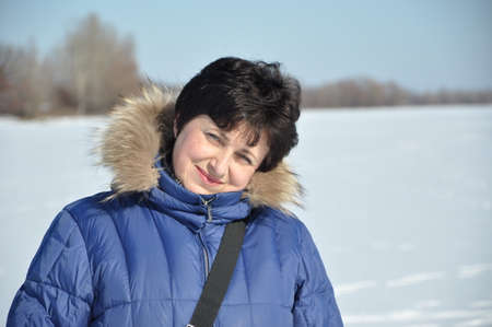 pretty cute young brunette woman in blue winter coat with fur sunny cold winter day on natural white...