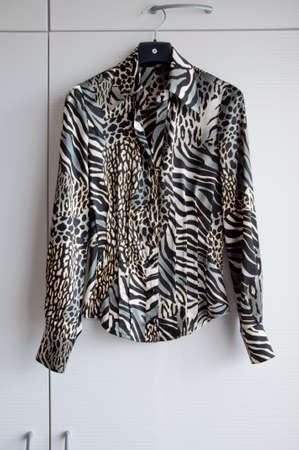 animal print silk or satin female blouse hanging on hanger in wardrobe or fashionable shop in show room on white backgroundの写真素材