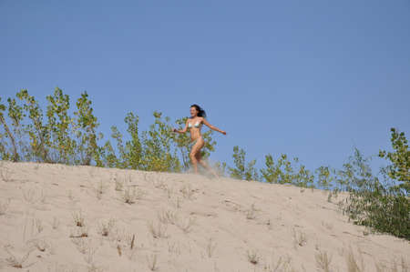 young pretty woman or cute girl with sexy body in swimsuit running on sand beach sunny outdoor on summer vacation, has smiling face and long brunette hairの写真素材