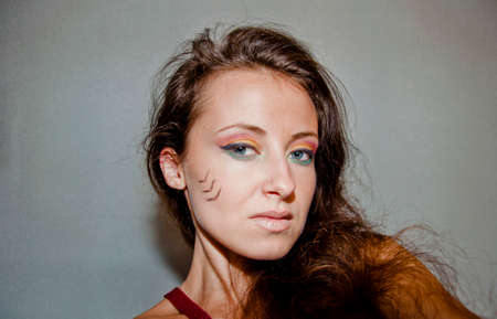 young cute sexy woman or girl with pocahontas ethnic tribal fashionable makeup on pretty face with long brunette hair on grey background, portraitの写真素材