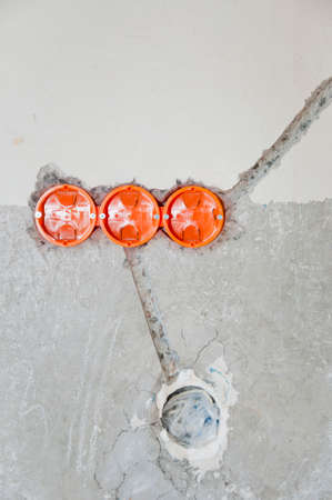 Holes in the wall with orange wires for socket switches. Man installing electricity. Maintenance repair works renovation in the flat. Restoration indoors. repair the apartment. electrical wiring.の写真素材