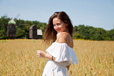 glad woman in white dress at ukrainian field of wheat crop spikelet with mill.の写真素材