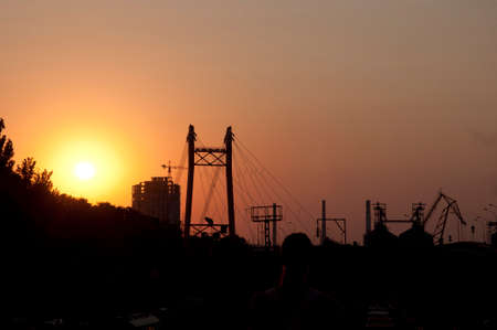 Urban landscape of electricity pylon structure and construction crane silhouettes at sunset sky background.の写真素材