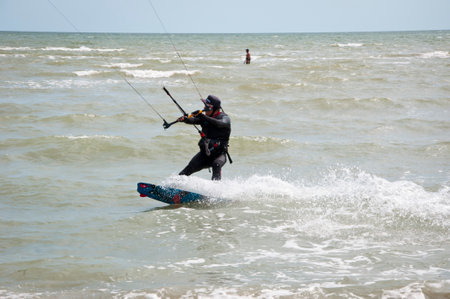 Henichesk, Ukraine - July 12, 2021: Surfer in wetsuit do trick. Kitesurfing athlete on kite board....