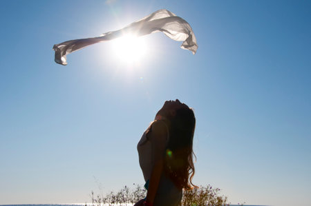 Levitating fabric. Girl dancing with flying fabric in backlit. Flying fluttering fabric and woman silhouette in the sun. Ballerina dancing with silk fabric. Ballet dancer in fluttering waving cloth.の写真素材
