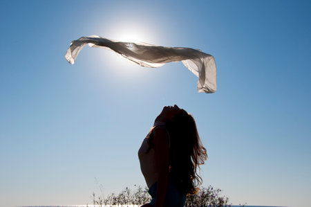 Levitating fabric. Girl dancing with flying fabric in backlit. Flying fluttering fabric and woman silhouette in the sun.の写真素材