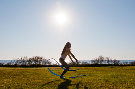 Flexible girl in summer sea. Woman silhouette with gymnastics ribbon. Sport flexibility. Gymnast hold ribbon in backlit. Gymnastics flexibility. Competitionの写真素材