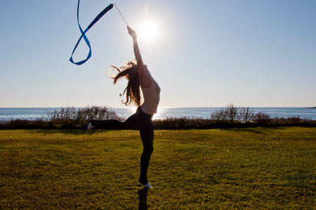 Flexible girl in summer sea. Woman silhouette with gymnastics ribbon. Rhythmic gymnast performing yoga. Sport athlete. Gymnast hold ribbon in backlit. Gymnastics flexibility.の写真素材