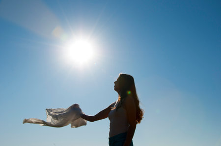 Girl dancing with flying fabric in backlit. Flying fluttering fabric and woman silhouette in the sun. Girl dancing with silk fabric. Dancer in fluttering waving cloth outside.の写真素材