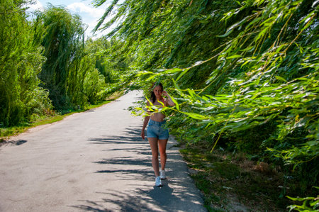 Woman walking on rural path. Summer countryside stroll. Outdoor lifestyle in nature. Willow tree branches in the breeze. Woman walks on rural road among willow tree branch in wind on summer. Quiet road.の写真素材