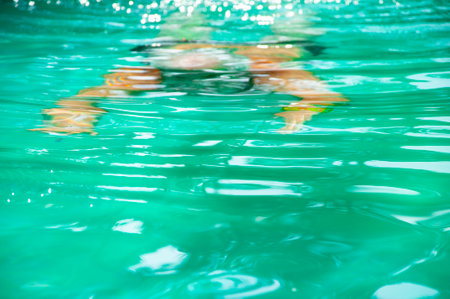 Pool dive by person man diver. Man diver diving in water of swimming pool and swim underwater. Vacation on summer. Diving in swimming pool. Summer vacation. Rippled water.の写真素材