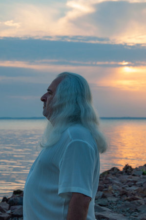 Retired man enjoying peaceful seaside evening. Senior traveler relaxing by the coast at golden hour....