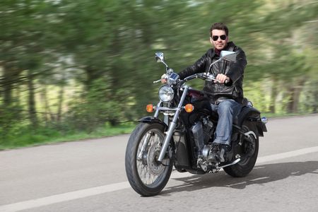 Young rider driving his cruiser-type motorcycle on the country road.