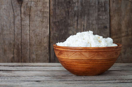 Cottage cheese on a wooden background. Fresh cottage cheese in ceramic dish on wooden boards. Dairy...