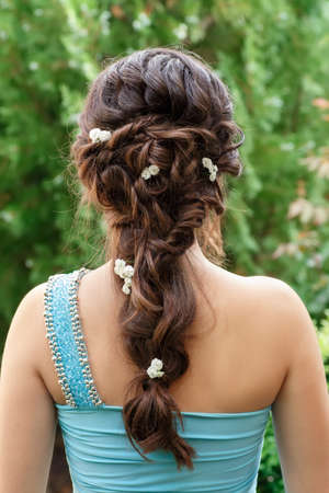 elegant hairstyle with fresh flowers in a plait . Woman with fashion festive hairstyle on nature...
