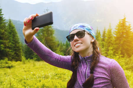girl in the mountains makes selfie. Hiker makes a selfie uses the phone. Traveler make selfie on...