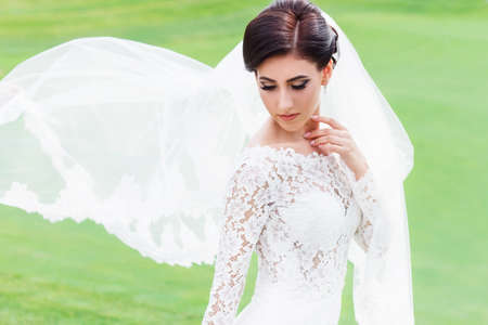 portrait of beautiful bride in wedding dress with fluttering veil on the green field of the golf club. Bride with long veil fluttering in the wind. Wedding, magazine, advertising, model, banner, poster dress, brideの写真素材
