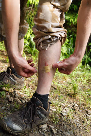 man apply aid plaster on leg. Leg with a plasters for wound, man provides first-aid self. Wound sealed with plaster. Man has scraped his leg outdoors and puts a sticking plaster on woundの写真素材