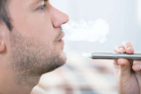 Young man smoking electronic cigarette. Closeup portrait of bearded man smoking an e-cigarette. Man...
