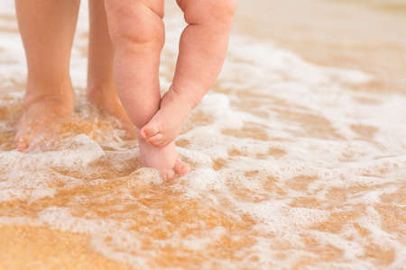 legs of female and baby on sea beach