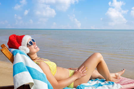 beautiful young woman in santa hat and sunglasses relaxing on sun lounger