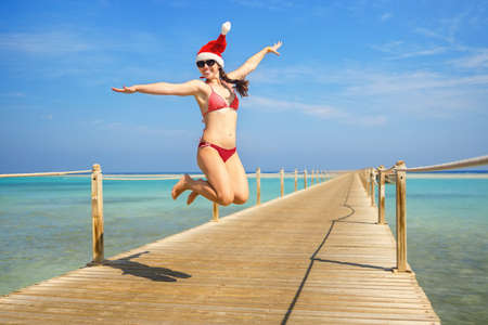 happy young woman in santa hat have fun and jumping on wooden pontoonの写真素材